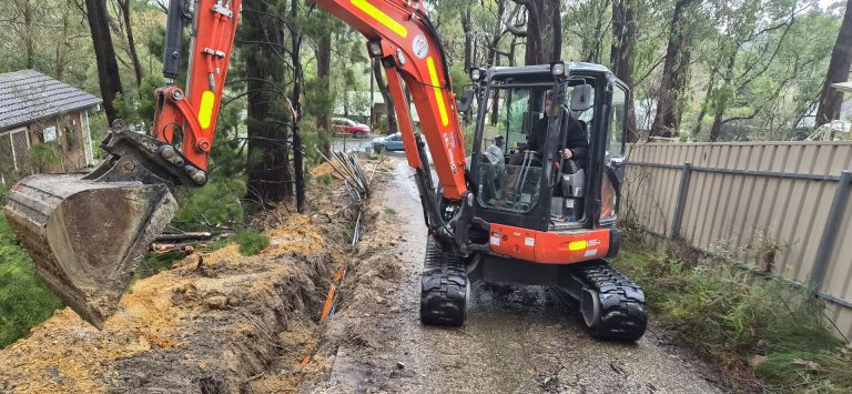 Excavator digging a cable trench alongside a residential driveway